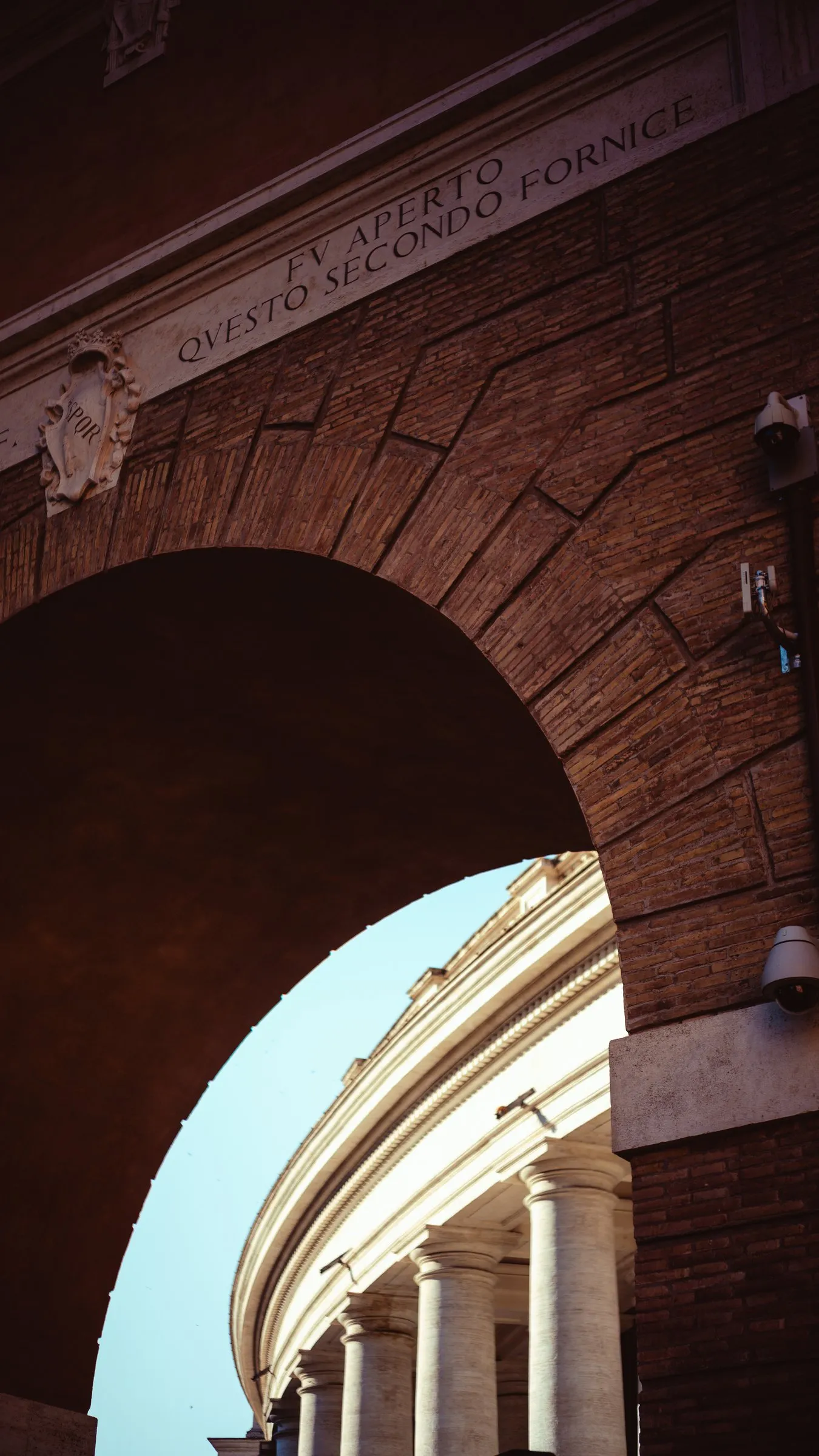 A nun in a white habit walks past the corner of a stone building, beneath a framed painting of the Madonna set into the façade.
