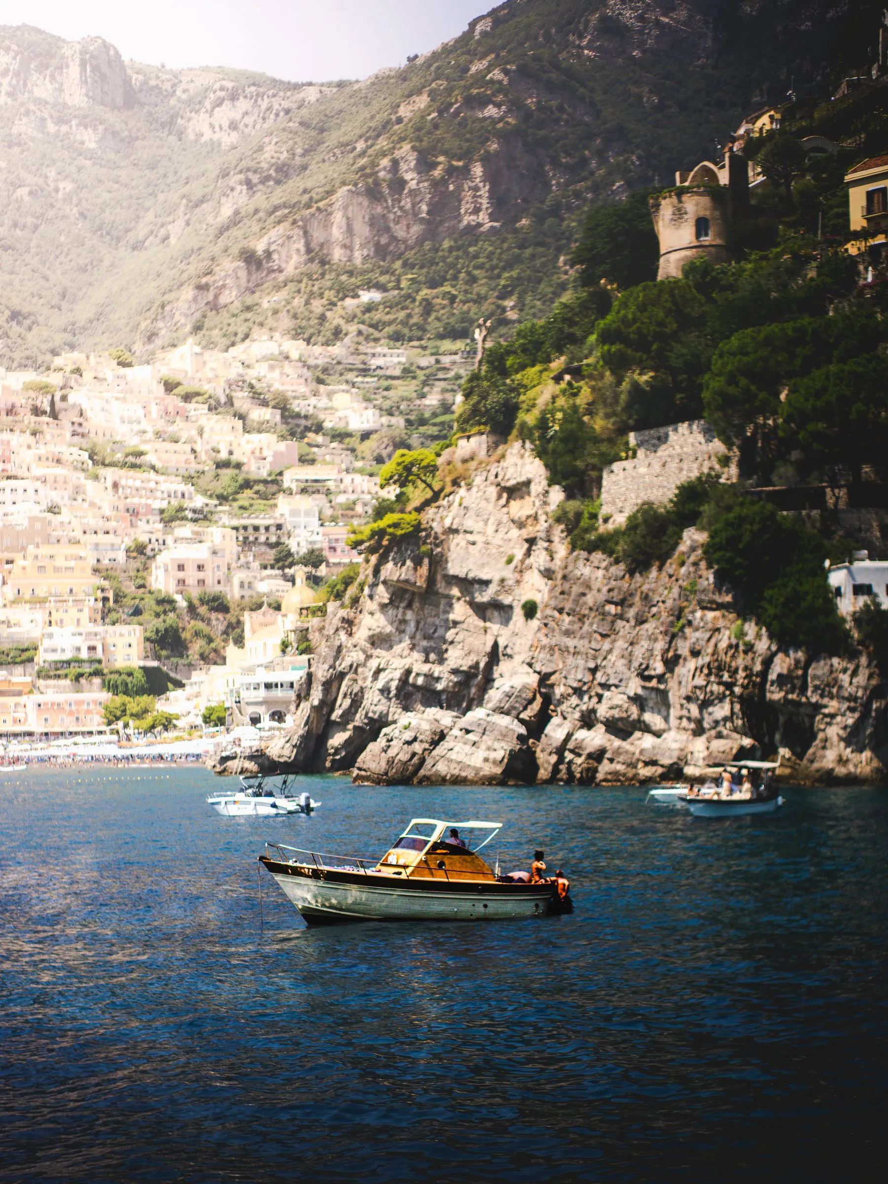 A woman in sunglasses looks back over her shoulder at the rail of a moving boat, deep blue water below.